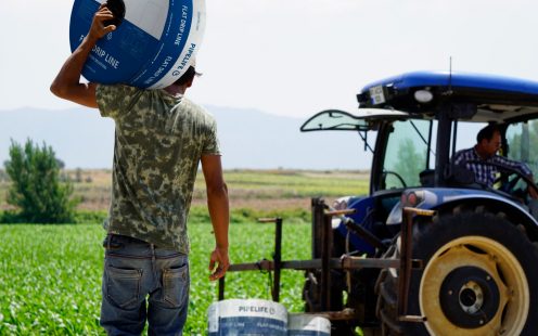 A farmer carrying a coiled Pipelife drip irrigation tape toward his tractor | Pipelife